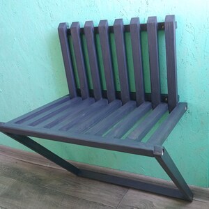 May include: A dark gray wooden bench with a slatted back and a rectangular seat. The bench is mounted to a wall and has a diagonal support brace.