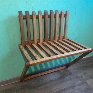 May include: A wooden wall-mounted bench with a slatted design. The bench is made of natural wood with a light brown finish.