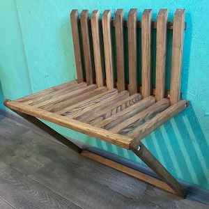 May include: A wooden wall-mounted bench with a slatted back and a folding design. The bench is made of natural wood with a light brown finish.