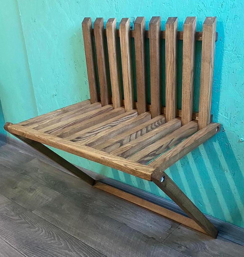 May include: A wooden wall-mounted bench with a slatted back and a folding design. The bench is made of natural wood with a light brown finish.