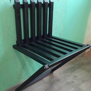 May include: A black wooden folding wall-mounted bench. The bench is made of slats and has a simple design.