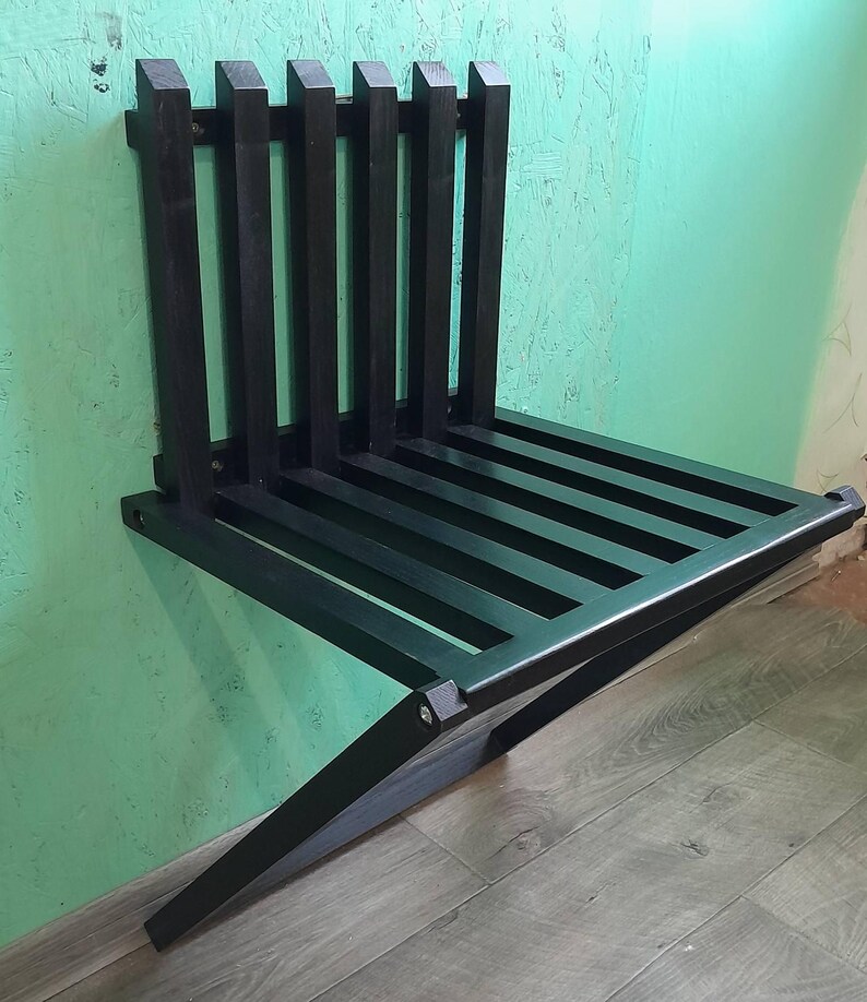 May include: A black wooden folding wall-mounted bench. The bench is made of slats and has a simple design.