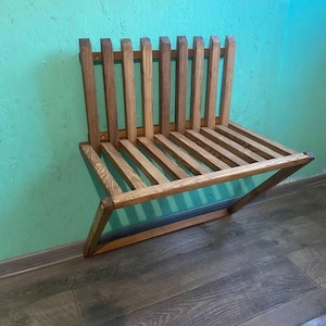 May include: A wooden wall-mounted bench with a slatted design. The bench is made of light brown wood and has a natural finish. It is mounted on a turquoise wall.