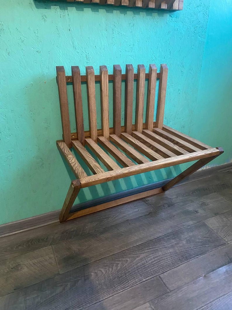 May include: A wooden wall-mounted bench with a slatted design. The bench is made of light brown wood and has a natural finish. It is mounted on a turquoise wall.