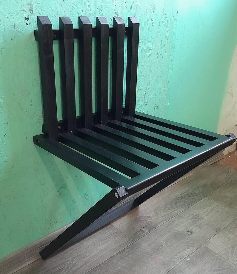 May include: A black wooden folding wall-mounted bench. The bench is made of slats and has a simple design.