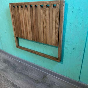 May include: A wooden headboard with a slatted design and a light brown finish. The headboard is mounted on a turquoise wall.
