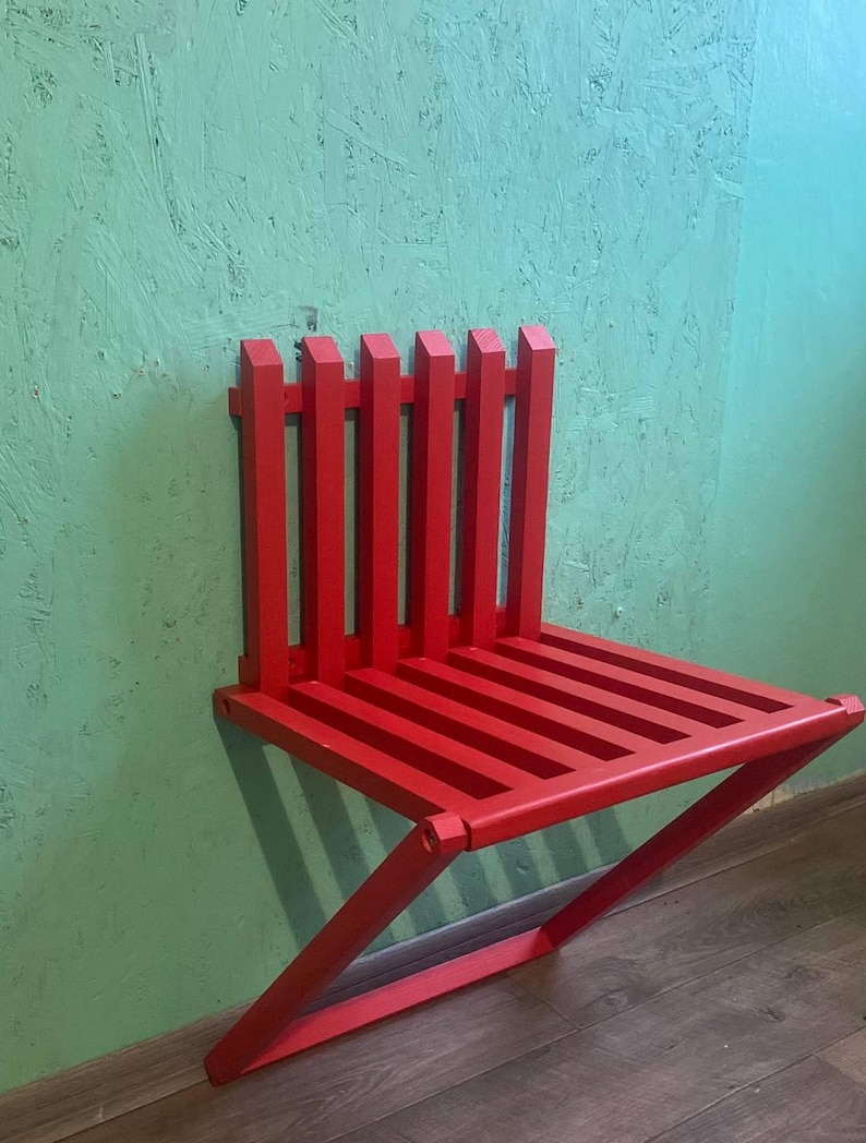 May include: A bright red, wooden, folding wall-mounted chair. The chair is made of slats and has a simple, modern design.