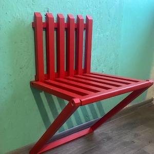 May include: A bright red folding wall-mounted chair with a slatted seat and back. The chair is made of wood and has a simple, modern design.