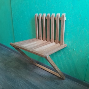 Könnte beinhalten: Eine an der Wand montierte, klappbare Holzbank mit einer hellen Holzoptik. Die Bank ist an einer türkisfarbenen Wand zusammengeklappt.