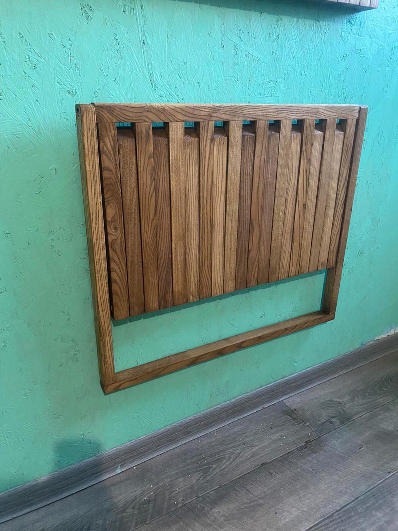 May include: A wooden wall-mounted folding table with a light brown stain. The table is made of slats and has a simple design.