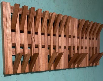 May include: A wooden wall-mounted coat rack with a unique design. The rack is made of light brown wood and features multiple angled hooks. The design is modern and geometric, with a series of vertical and angled wooden pieces.