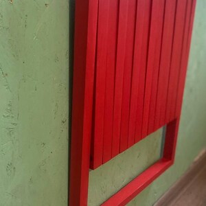 May include: A red wooden folding chair is mounted to a green wall. The chair is folded and has a simple design.