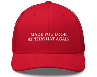 May include: Red mesh trucker hat with white embroidered text that reads "MADE YOU LOOK AT THIS HAT AGAIN".