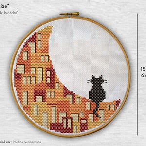 May include: A black cat sitting on a crescent moon-shaped embroidery pattern with orange, yellow, and red colours. The embroidery is framed in a wooden hoop with a 6x8 inch size.