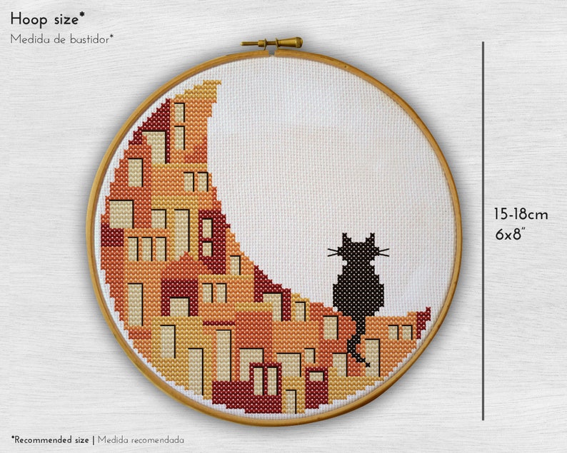 May include: A black cat sitting on a crescent moon-shaped embroidery pattern with orange, yellow, and red colours. The embroidery is framed in a wooden hoop with a 6x8 inch size.