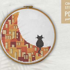 May include: Cross stitch pattern featuring a black cat sitting on a crescent moon shaped design with orange, yellow, and red houses.