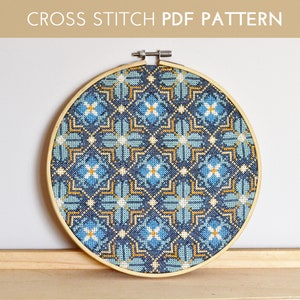 Puede incluir: Un patrón de punto de cruz azul, amarillo y blanco en un aro de bordado de madera. El patrón presenta un diseño geométrico con cuadrados y flores que se repiten.
