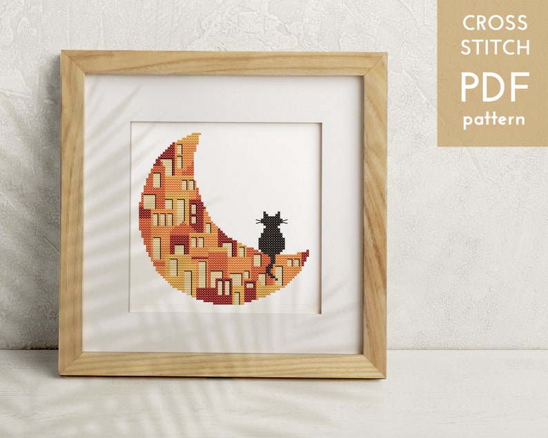 May include: A cross stitch pattern featuring a black cat sitting on a crescent moon with a cityscape design. The moon is filled with orange, yellow, and red houses.