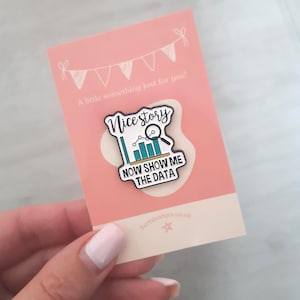 May include: A badge with the text "Nice story" and "NOW SHOW ME THE DATA" on a pink card. The badge features a chart and magnifying glass design. The card also has the text "A little something just for you!"
