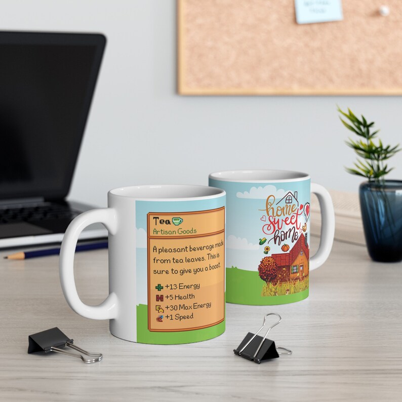 May include: Two white ceramic mugs. One mug features a cartoon illustration of a house with the text "home sweet home". The other mug features a video game-style card with the text "Tea Artisan Goods" and a description of the item's effects.