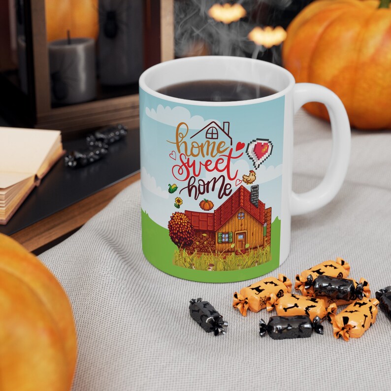 May include: White ceramic mug with a blue, green, and brown illustration of a house with the text "home sweet home". The mug is filled with coffee and steam is rising from the top.