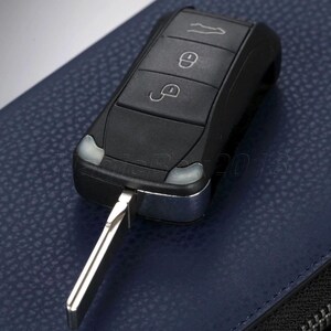 Puede incluir: Llave de coche negra con detalles plateados y llave plegable. La llave tiene tres botones con iconos para bloquear, desbloquear y abrir el maletero. Sobre una superficie de cuero azul.
