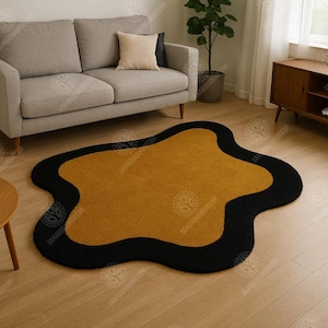 May include: Mustard yellow and black area rug with an organic, free-form shape. The rug has a mustard yellow center with a thick black border. The rug is placed on a light wood floor in a living room setting.