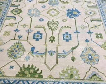 May include: A beige area rug with a detailed floral pattern in shades of blue and green. The rug features a central design with symmetrical floral motifs and a border with geometric patterns. The overall design is intricate and detailed, suitable for home decor.