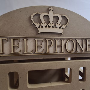 May include: A wooden model of a classic red telephone box with a crown on top and the word "TELEPHONE" on the front.
