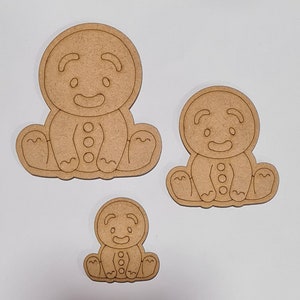 May include: Three unfinished wooden gingerbread man ornaments of varying sizes. The gingerbread men are sitting with their arms crossed and have a simple smiling face.