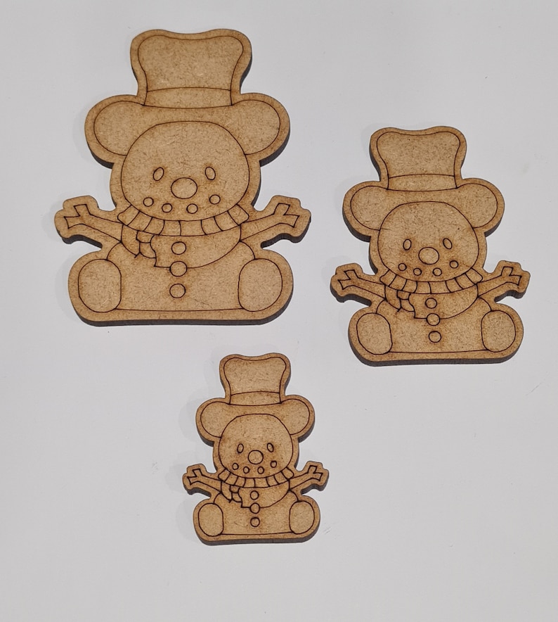 May include: Three wooden snowman decorations of varying sizes. Each snowman has a hat, scarf, and buttons. The decorations are unfinished and ready to be painted.