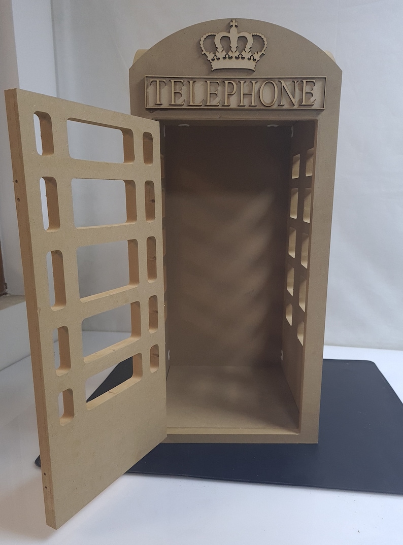 May include: A wooden model of a red British telephone box with a crown on top and the word "TELEPHONE" on the front. The door is open and the inside is empty.
