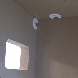 May include: Close-up of a white corner bracket attached to a light brown wall. The bracket is designed to hold a shelf.