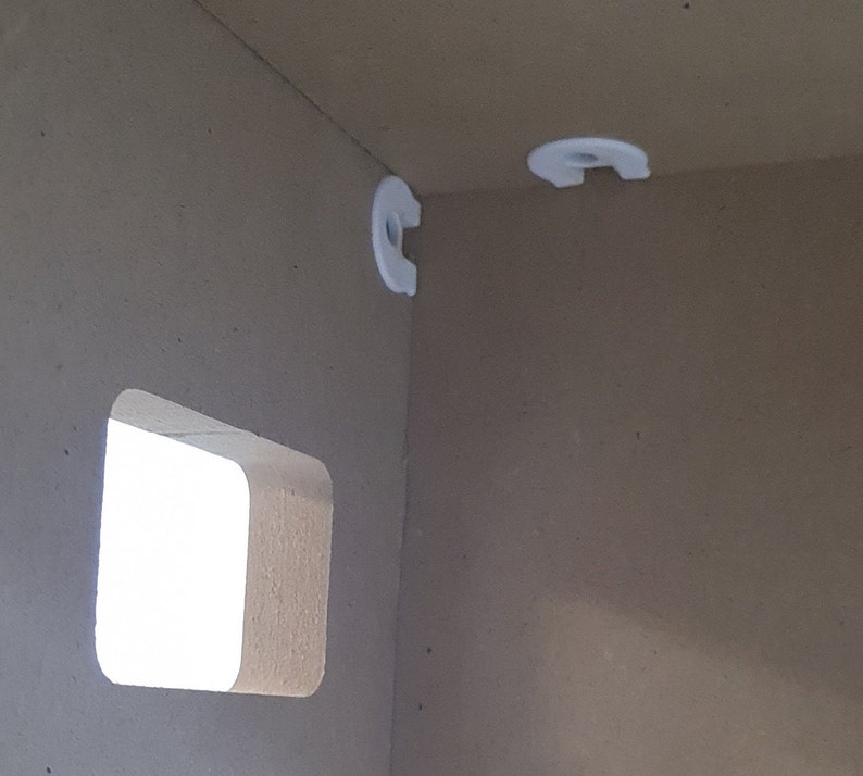 May include: Close-up of a white corner bracket attached to a light brown wall. The bracket is designed to hold a shelf.