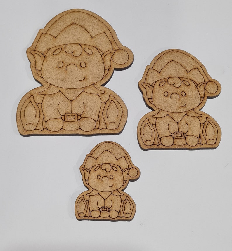 May include: Three unfinished wooden elf ornaments in various sizes. The elves are wearing pointy hats and have big eyes and smiles. They are holding small bags in their hands.