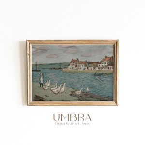 May include: A framed vintage print depicts a coastal scene with a body of water, buildings, and several white geese. A person stands near the geese. The print is in a gold-colored frame. The text "UMBRA Digital Wall Art Prints" is at the bottom.