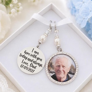May include: A memorial charm set featuring two circular pendants hanging from a white ribbon. One silver-toned pendant displays the text: I am here with you today and always. Love, Dad 07/09/2027. The other pendant features a photograph of an older man.