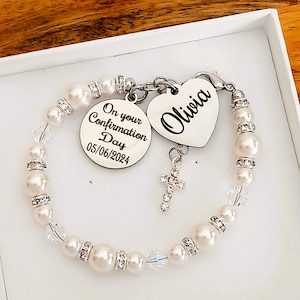 May include: A white pearl bracelet with a silver charm that says "On your Confirmation Day 05/06/2024" and a silver heart charm that says "Olivia".