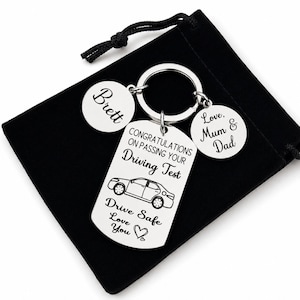 May include: A silver-colored keychain with a car design and the text "CONGRATULATIONS ON PASSING YOUR Driving Test." Includes round charms with the names "Brett" and "Love, Mum & Dad." The keychain rests on a black velvet pouch.