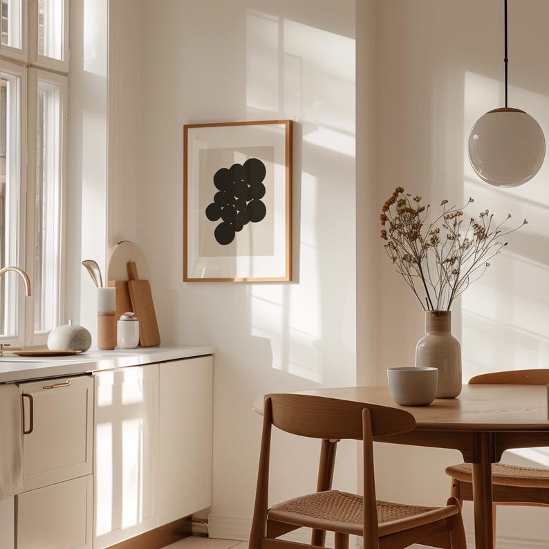 Puede incluir: Una l&aacute;mina de arte mural enmarcada que presenta un grupo de c&iacute;rculos negros sobre un fondo beige claro, expuesta en una cocina con una mesa de comedor de madera, sillas con asientos trenzados, una l&aacute;mpara colgante blanca y un jarr&oacute;n con flores secas.