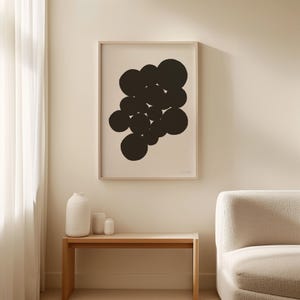 Puede incluir: Una l&aacute;mina de arte enmarcada que presenta un grupo de c&iacute;rculos negros s&oacute;lidos de varios tama&ntilde;os dispuestos en un patr&oacute;n abstracto sobre un fondo beige claro, exhibida en un marco de madera fino colgado en la pared sobre una mesa consola.