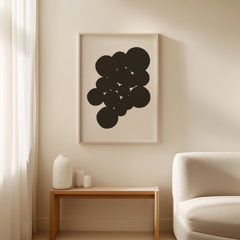 Puede incluir: Una l&aacute;mina de arte enmarcada que presenta un grupo de c&iacute;rculos negros s&oacute;lidos de varios tama&ntilde;os dispuestos en un patr&oacute;n abstracto sobre un fondo beige claro, exhibida en un marco de madera fino colgado en la pared sobre una mesa consola.