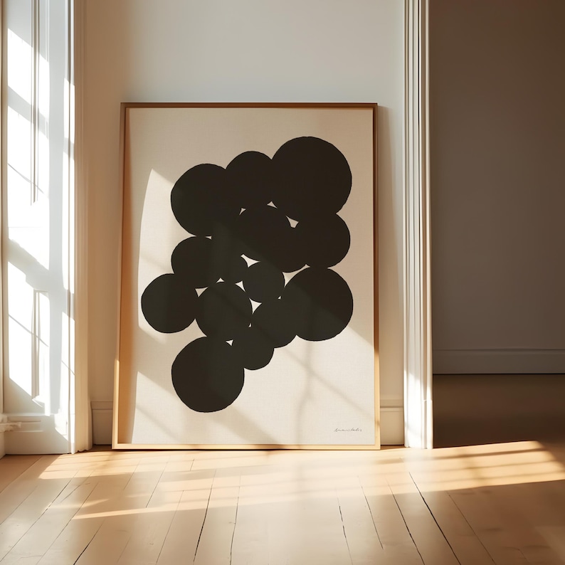 Puede incluir: Una pieza de arte mural rectangular enmarcada que presenta un grupo de c&iacute;rculos negros s&oacute;lidos dispuestos en un patr&oacute;n abstracto sobre un fondo color crema. La obra est&aacute; encerrada en un marco de madera fina y clara con una firma en la esquina.