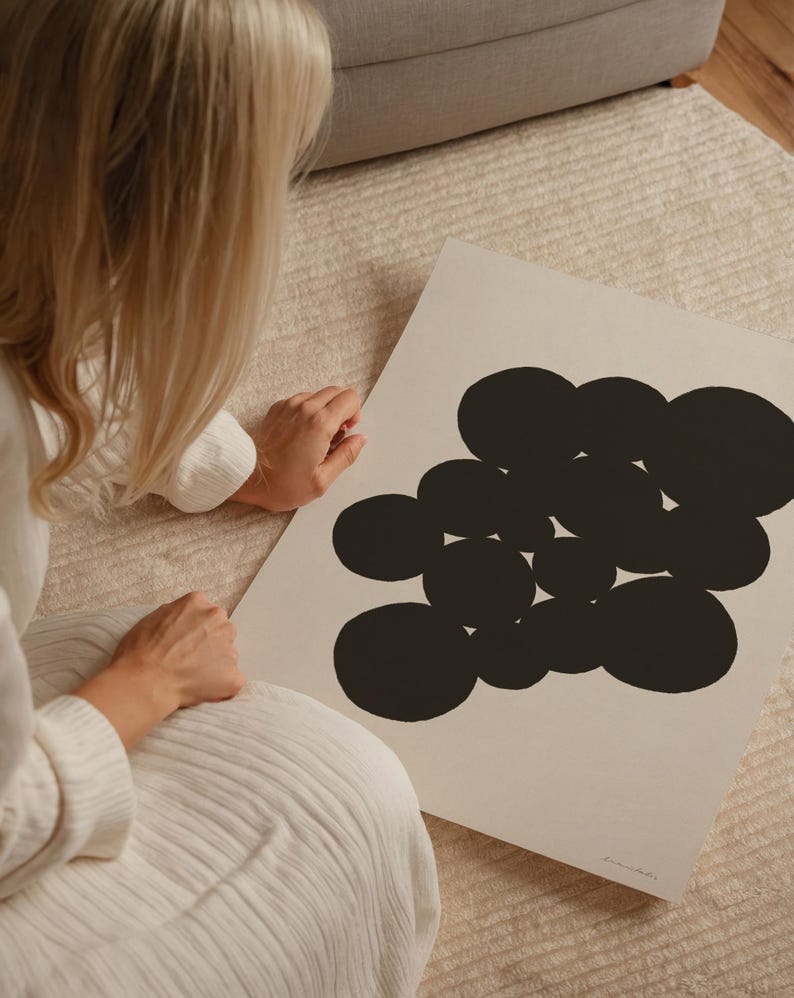 Puede incluir: Una l&aacute;mina de arte rectangular sobre un fondo beige claro que presenta un grupo de c&iacute;rculos negros s&oacute;lidos de tama&ntilde;os variados dispuestos en una formaci&oacute;n densa y org&aacute;nica. La l&aacute;mina incluye una peque&ntilde;a firma tenue en la esquina inferior derecha.
