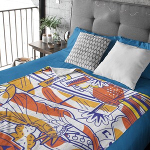 May include: A white fleece throw blanket with a colorful graphic design featuring a stylized image of the Statue of Liberty, a yellow taxi cab, and the text "BROADWAY" and "AVENUE".