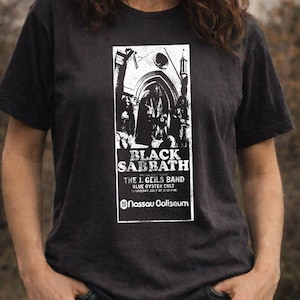 May include: Dark grey t-shirt with a white graphic of a Black Sabbath concert poster. The poster includes the band's name, supporting acts, and venue: Nassau Coliseum. The shirt has a crew neck.