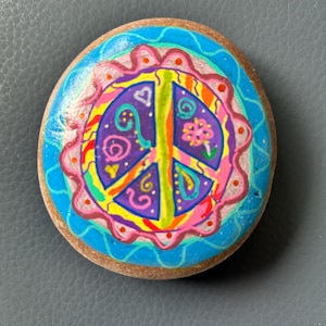 Hand painted brightly coloured peace sign on a natural beach stone