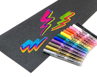 Op de afbeelding: Een set van 12 metallic verfmarkeringen met een zwarte grip en een zilveren dop. De markeringen zijn in een rij gerangschikt, met de doppen naar de kijker gericht. De markeringen zijn gelabeld "Crayola Paint Markers". De markeringen bevinden zich op een zwart oppervlak met een bliksemontwerp dat in verschillende kleuren is getekend.