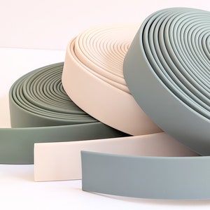 Può includere: Tre rotoli di passamaneria in tessuto di diversi colori: verde salvia, rosa chiaro e blu chiaro. La passamaneria è arrotolata e le estremità sono visibili.
