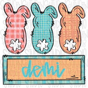 Op de afbeelding: Drie paashaasuitsparingen in roze ruit, blauwe stippen en oranje ruit, elk met een witte, pluizige staart. Daaronder een rechthoekig bord met de naam "Demi" in turquoise script.